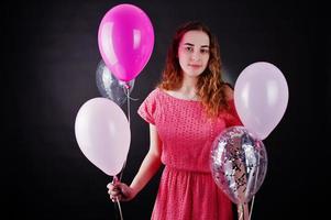 Young girl in red dress with balloons against black background on studio. photo