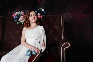 Pretty young gilrl musician in white dress with double bass sitting on brown vintage sofa. photo