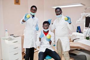 tres colegas médicos afroamericanos en una clínica dental con manzanas en las manos. foto