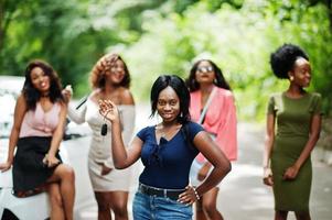 Group of five happy african american girls posed against car, one of them show keys. photo