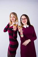 Two attractive friends in purple dresses drink sparkling wine or champagne in the studio. photo