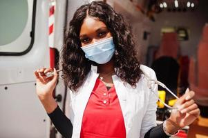 paramédica afroamericana con mascarilla médica protectora frente al camión de la ambulancia. foto