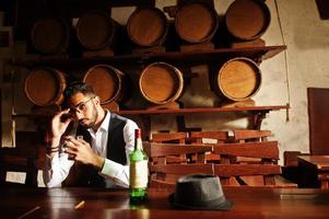 Handsome well-dressed arabian man with glass of whiskey and cigar posed at pub. photo