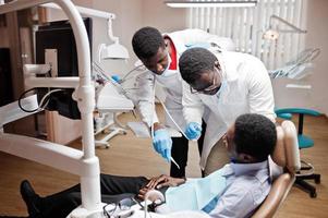 paciente afroamericano en silla dental. oficina de dentista y concepto de práctica médica. dentista profesional ayudando a su paciente en odontología médica. taladrar los dientes del paciente en la clínica. foto