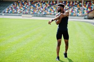 African american male athlete in sportswear doing stretching exercise at stadium. photo