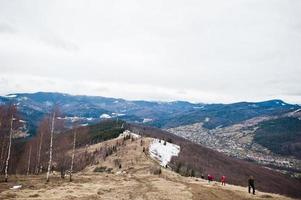 Tourists group hiking at snowy mountain valleys at Carpathian mountains. View of Ukrainian Carpathians and Yaremche from the top of Makovitsa. photo