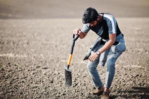 agricultor agrónomo del sur de asia con pala inspeccionando suelo negro. concepto de producción agrícola. foto