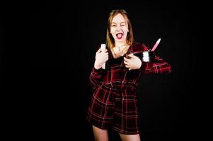 Young housewife in checkered dress with saucepan and kitchen spoon and bottle isolated on black background. photo