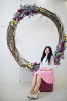 Young brunette girl in pink skirt and white blouse posed indoor against large decorated wreath. photo