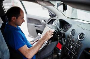 Car repair and maintenance theme. Electric mechanic in uniform working in auto service, making car diagnostics using obd device with laptop. photo