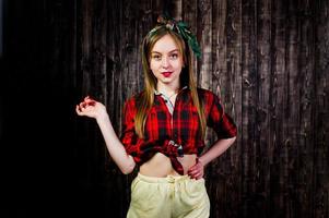 Young funny housewife in checkered shirt and yellow shorts pin up style on wooden background. photo