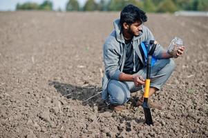 South asian agronomist farmer with shovel inspecting black soil. Agriculture production concept. photo