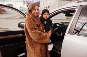 la joven madre y el niño se paran cerca de su auto todoterreno. concepto de conducción segura. foto