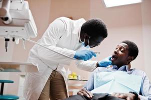 paciente afroamericano en silla dental. oficina de dentista y concepto de práctica médica. dentista profesional ayudando a su paciente en odontología médica. taladrar los dientes del paciente en la clínica. foto