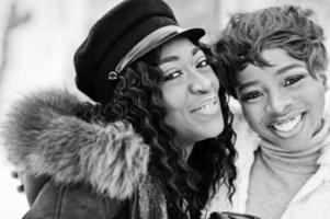 Close up faces of two african american womans in sheepskin and fur coat posed at winter day against snowy background. photo