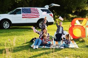 American family spending time together. With USA flags against big suv car outdoor. photo