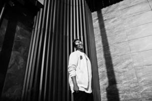 Stylish hipster arab man guy in sunglasses posed outdoor in street at sunset against gray wall. photo