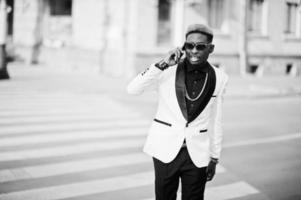 Chic handsome african american man in white suit walking on crosswalk and speaking on phone. photo