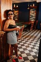 Portrait of african american woman, retro hairstyle posing at restaurant with cup of latte. photo