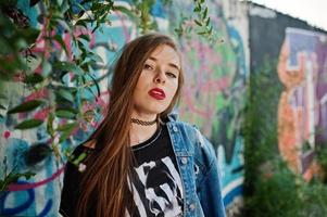 chica hipster casual con estilo en ropa de jeans y gafas contra una gran pared de graffiti. foto