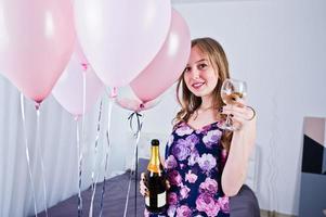 chica feliz con globos de colores en la cama en la habitación con copas y botella de champán. celebrando el tema del cumpleaños. foto