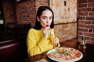 Funny brunette girl in yellow sweater eating pizza at restaurant. photo