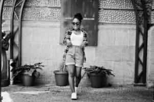 chica afroamericana de hip hop con gafas de sol y pantalones cortos. retrato casual de moda callejera de mujer negra. foto