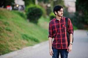 joven estudiante indio con camisa a cuadros roja y jeans con mochila posada en la calle. foto