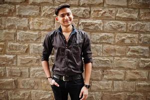 Indian man in brown shirt posed outdoor against brick background. photo