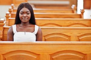 mujer afroamericana rezando en la iglesia. los creyentes meditan en la catedral y tiempo espiritual de oración. chica afro sentada en un banco.