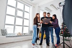 Photographer explaining about the shot to his team in the studio and looking on laptop. Talking to his assistants holding a camera during a photo shoot. Teamwork and brainstorm.