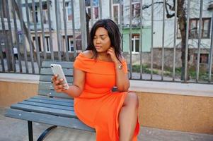 African american woman model xxl in orange dress looking on mobile phone. photo