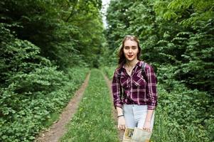 retrato de una joven y hermosa mujer rubia con camisa de tartán sosteniendo un mapa en el bosque. foto