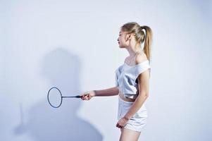 Chica caucásica morena de cuerpo sexy en forma increíble posando en el estudio sobre fondo blanco en pantalones cortos y top con raqueta de bádminton. foto