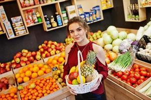 Girl in red holding different fruit and vegetables at basket on fruits store. photo