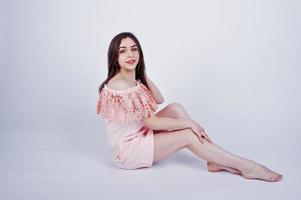 Portrait of a fashionable woman in pink dress sitting and posing on the floor in the studio. photo