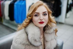 Elegance blonde girl in fur coat at the store of fur coats and leather jackets. photo