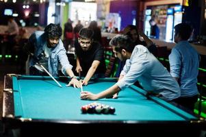 Group of stylish asian friends wear on jeans playing pool billiard on bar. photo