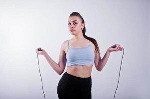 alegre y atractiva mujer joven en forma con polainas superiores y negras con cuerda para saltar aislada sobre fondo blanco. foto