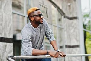 Stylish african american boy on gray sweater and black sunglasses posed at street. Fashionable black guy. photo