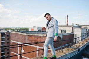 Dreamer stylish macho man in gray suit and glasses posed on the roof. photo