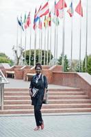 African student female posed with backpack and school items on yard of university, against flags of different countries. photo