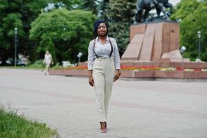 elegante mujer de negocios afroamericana en pantalones con tirantes y blusa posada al aire libre. foto