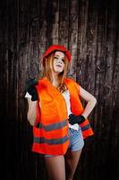 Engineer woman in orange protect helmet and building jacket against wooden background. photo