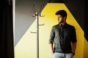 Confident young indian man in black shirt standing near yellow wall. photo