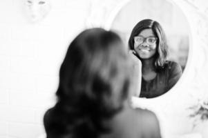 Pretty african american woman in eyeglasses posed in room against mirror. photo