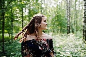 Portrait of a fabulous young girl in pretty dress with stylish curly hairstyle posing in the forest or park. photo