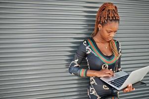 Portrait of handsome stylish african american model woman with laptop against grey steel shutter. photo