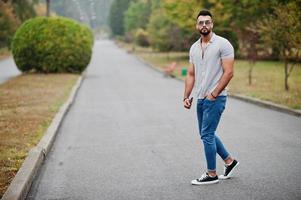 Fashionable tall arab beard man wear on shirt, jeans and sunglasses posed on park and hold wallet at hand. photo