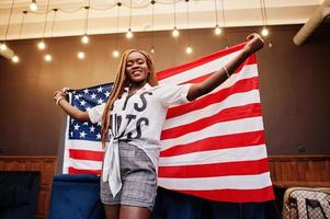 bella mujer africana con elegante ropa informal posando con la bandera de estados unidos en las manos en el cargo. foto